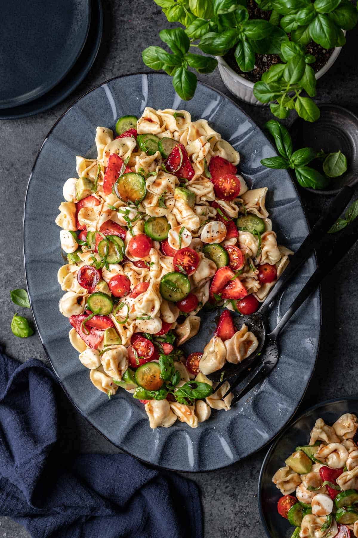 Summer tortellini caprese salad on a blue serving platter with black serving utensils.