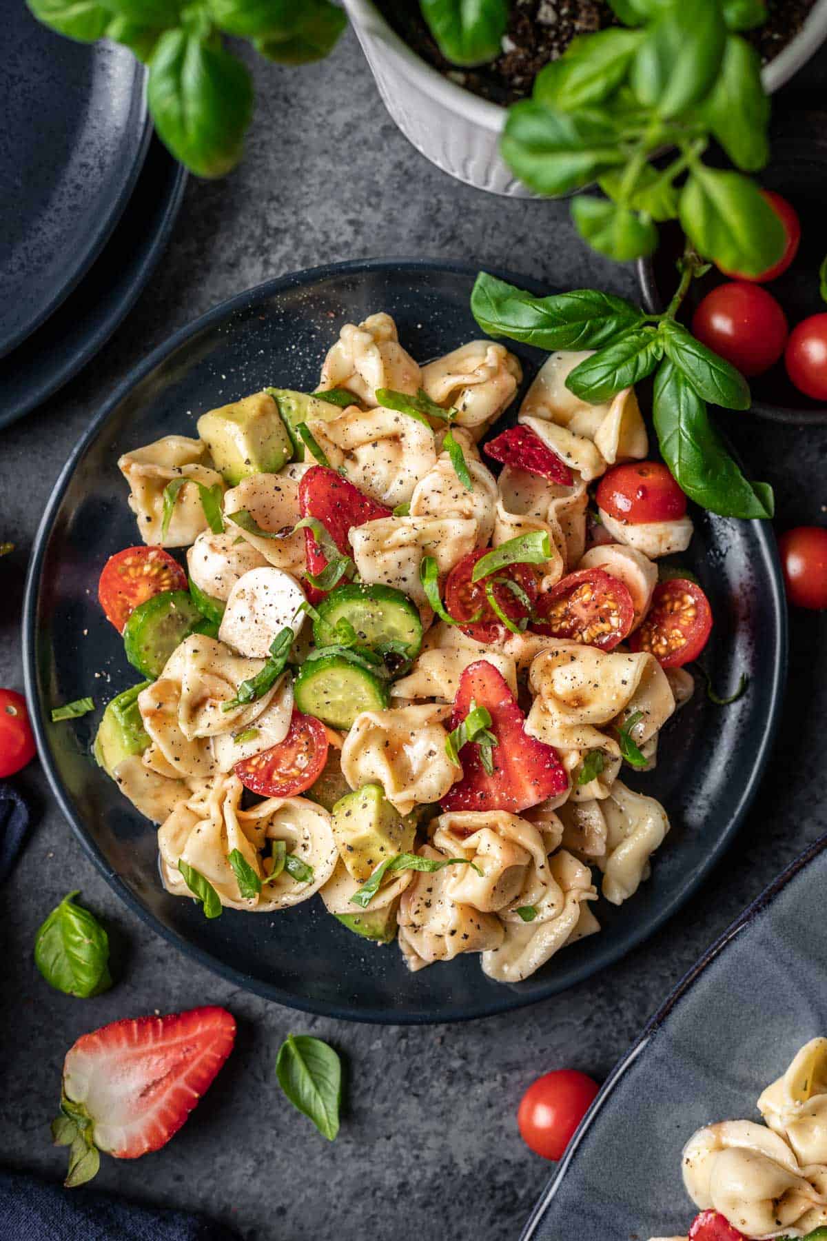 Summer tortellini caprese salad on a blue plate garnished with fresh basil.