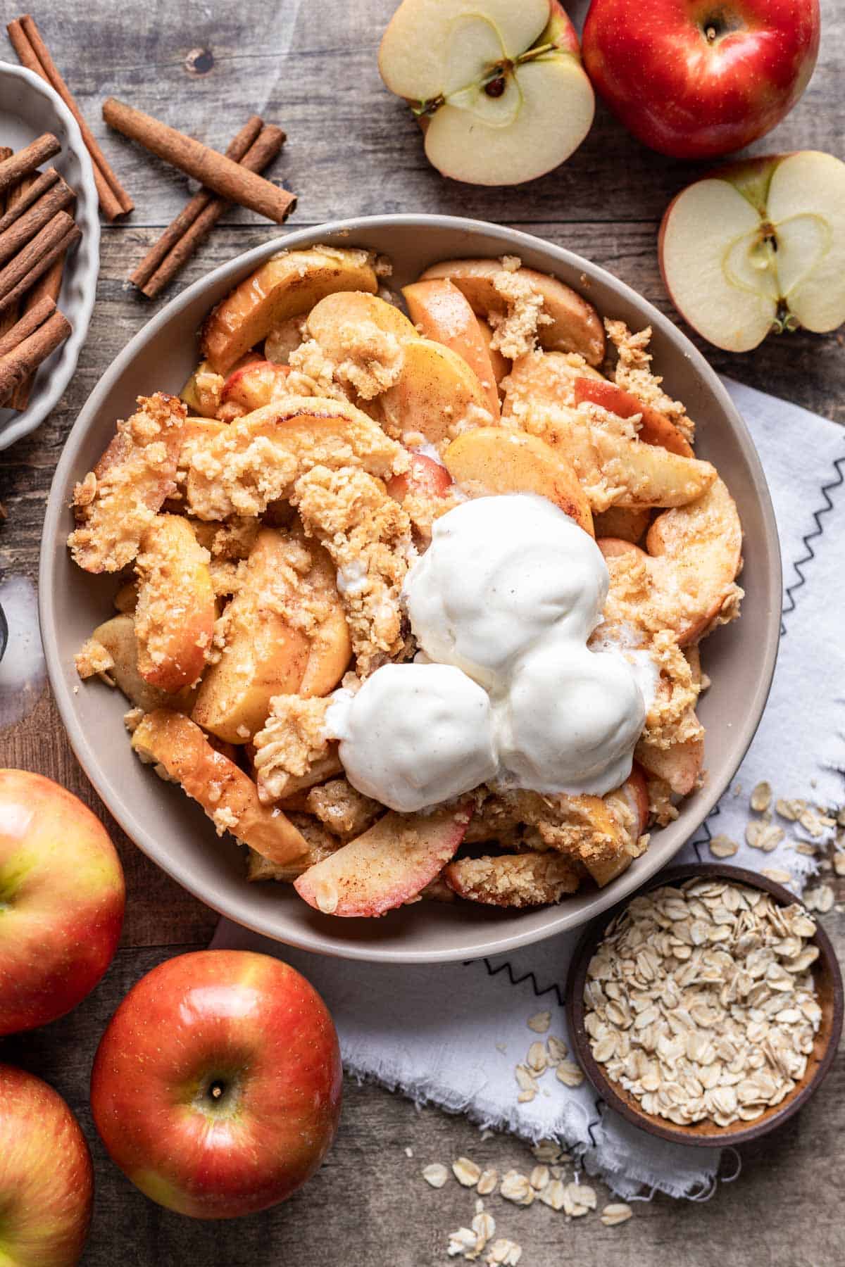 Air fryer apples topped with an oat crumble and scoops of vanilla ice cream.