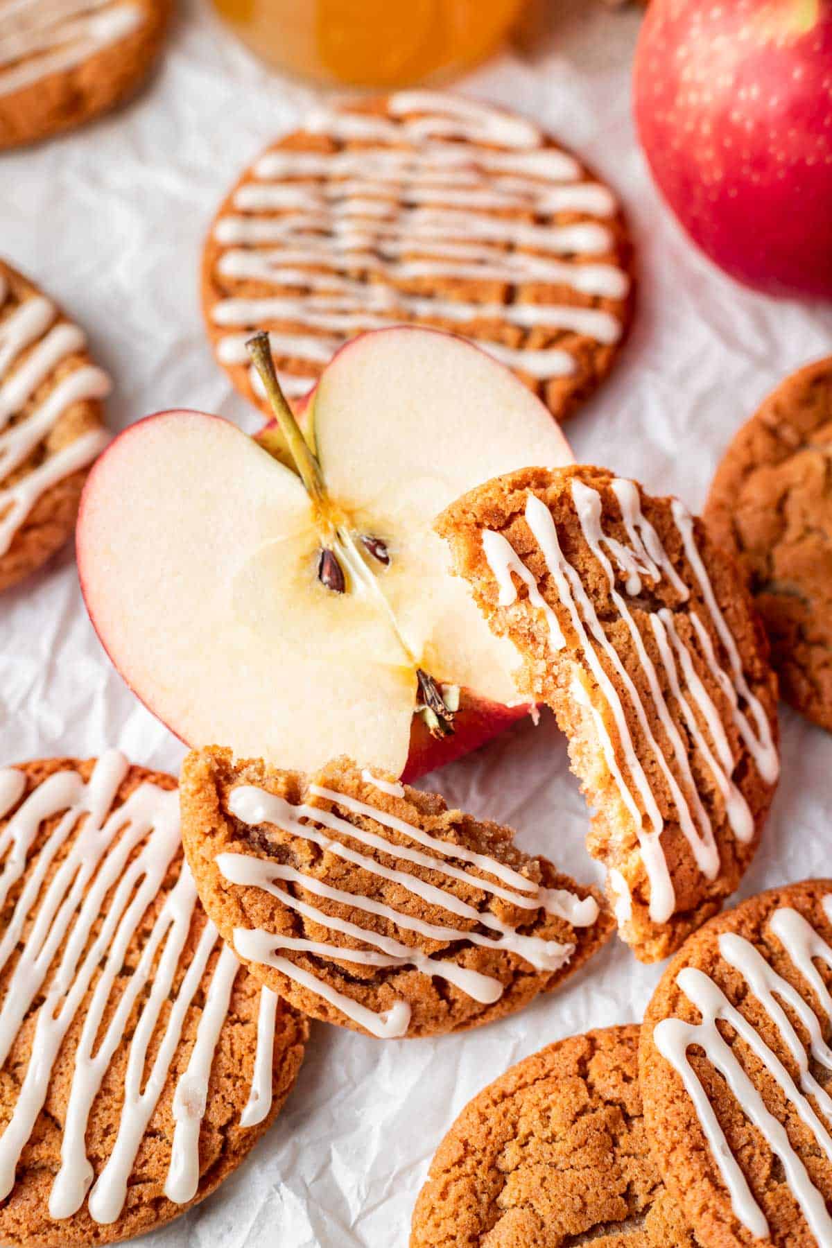 An apple cider cookie broken in half surrounded by apples.