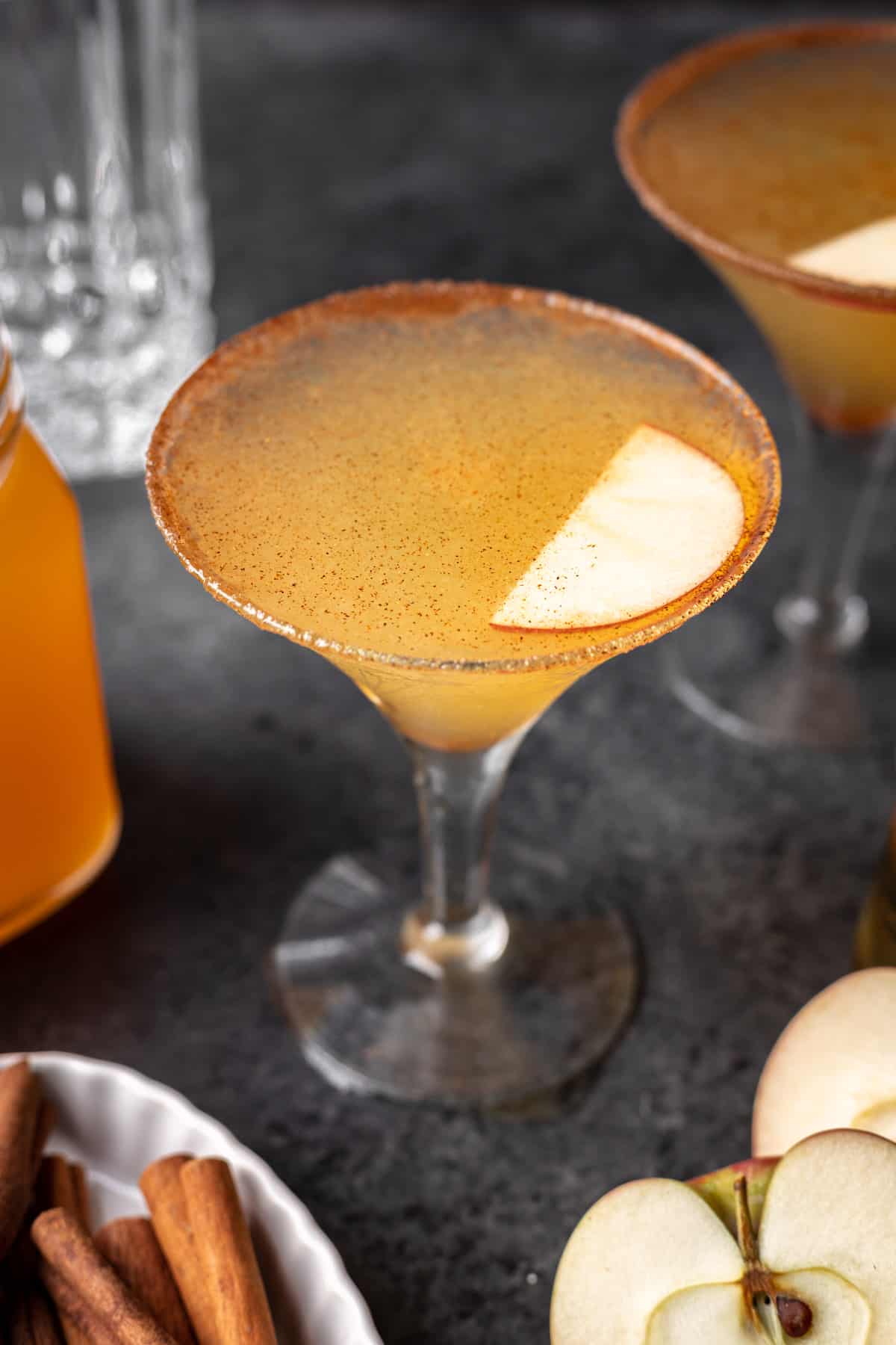 Apple cider martini garnished with ground cinnamon and a sliced apple.