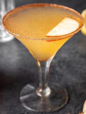 Apple cider martini garnished with ground cinnamon and an apple slice.