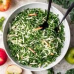 Kale apple slaw in a serving bowl with serving utensils.