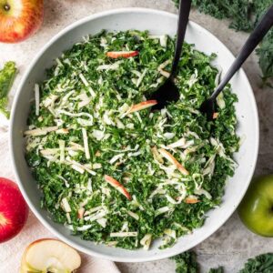 Kale apple slaw in a serving bowl with serving utensils.