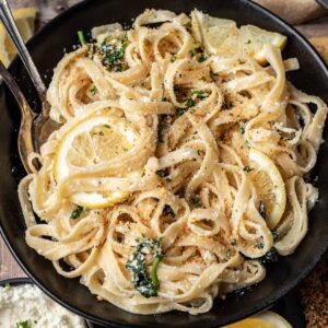 Lemon ricotta pasta in a black bowl with serving utensils.