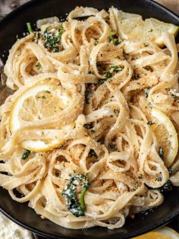 Lemon ricotta pasta in a black bowl with serving utensils.