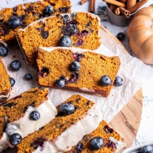 Sliced pumpkin blueberry bread with glaze and fresh blueberries on top.