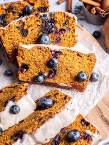 Sliced pumpkin blueberry bread with glaze and fresh blueberries on top.