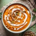 Pumpkin, carrot, sweet potato soup in a green bowl drizzled with coconut cream on top.