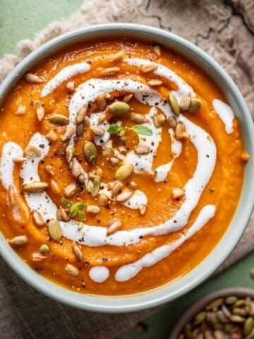 Pumpkin, carrot, sweet potato soup in a green bowl drizzled with coconut cream on top.