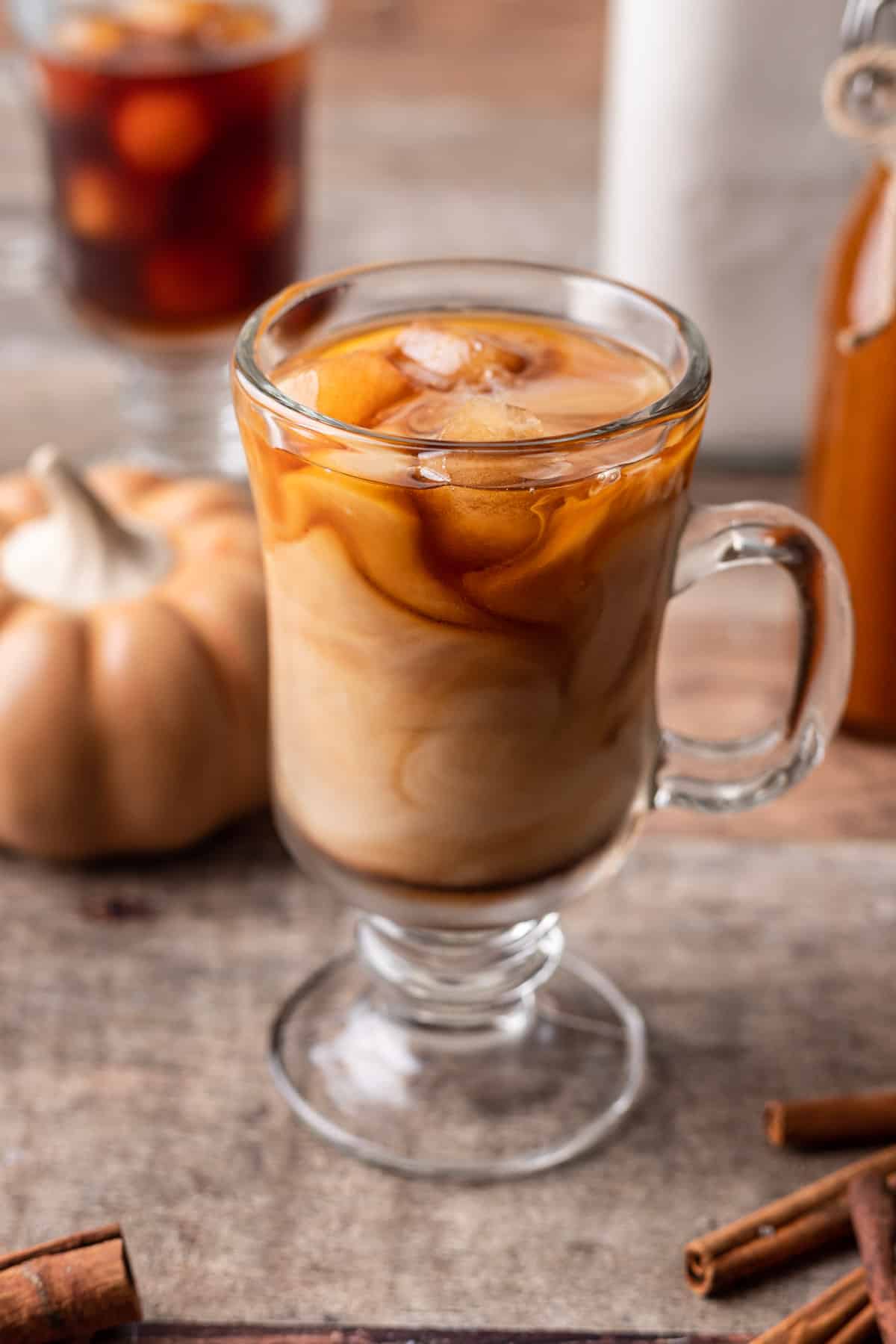 Iced pumpkin spice latte in a glass mug with coffee and milk swirling together.