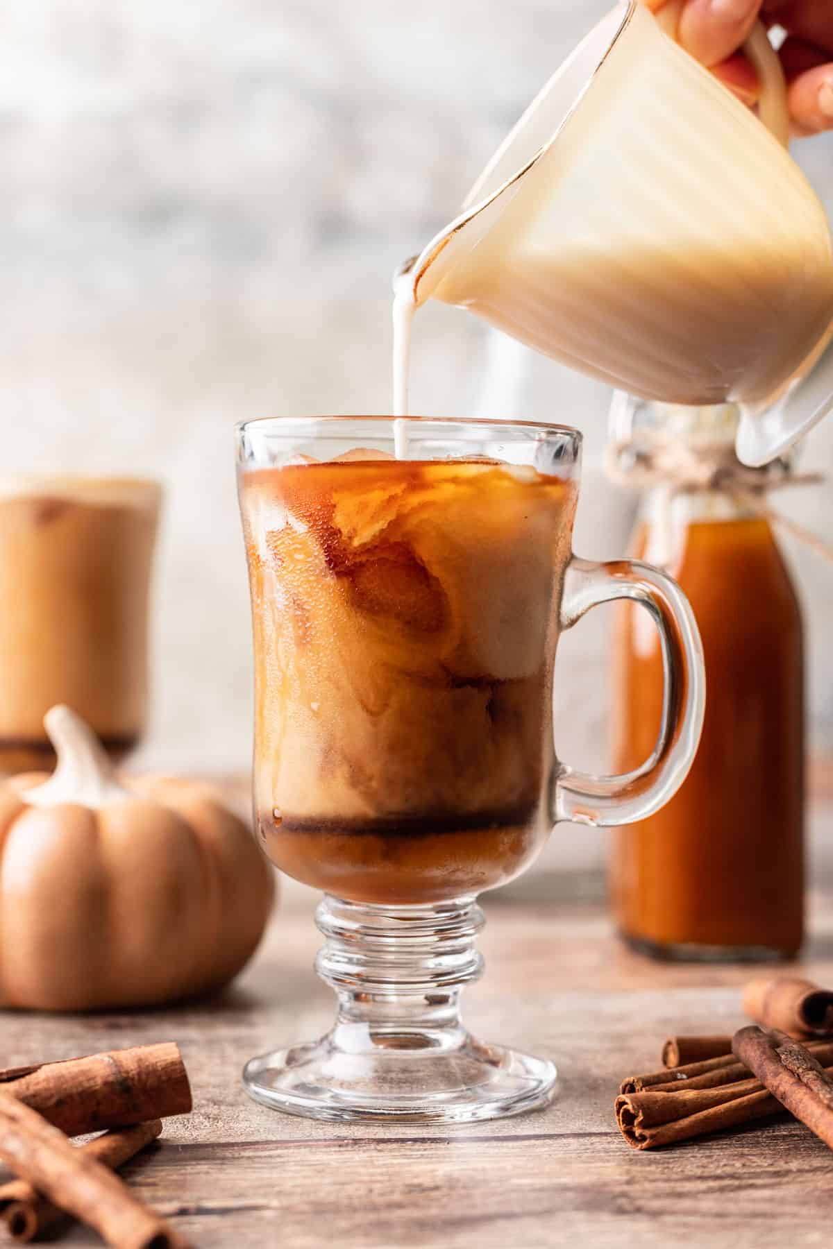 Pouring milk into an iced pumpkin spice coffee.