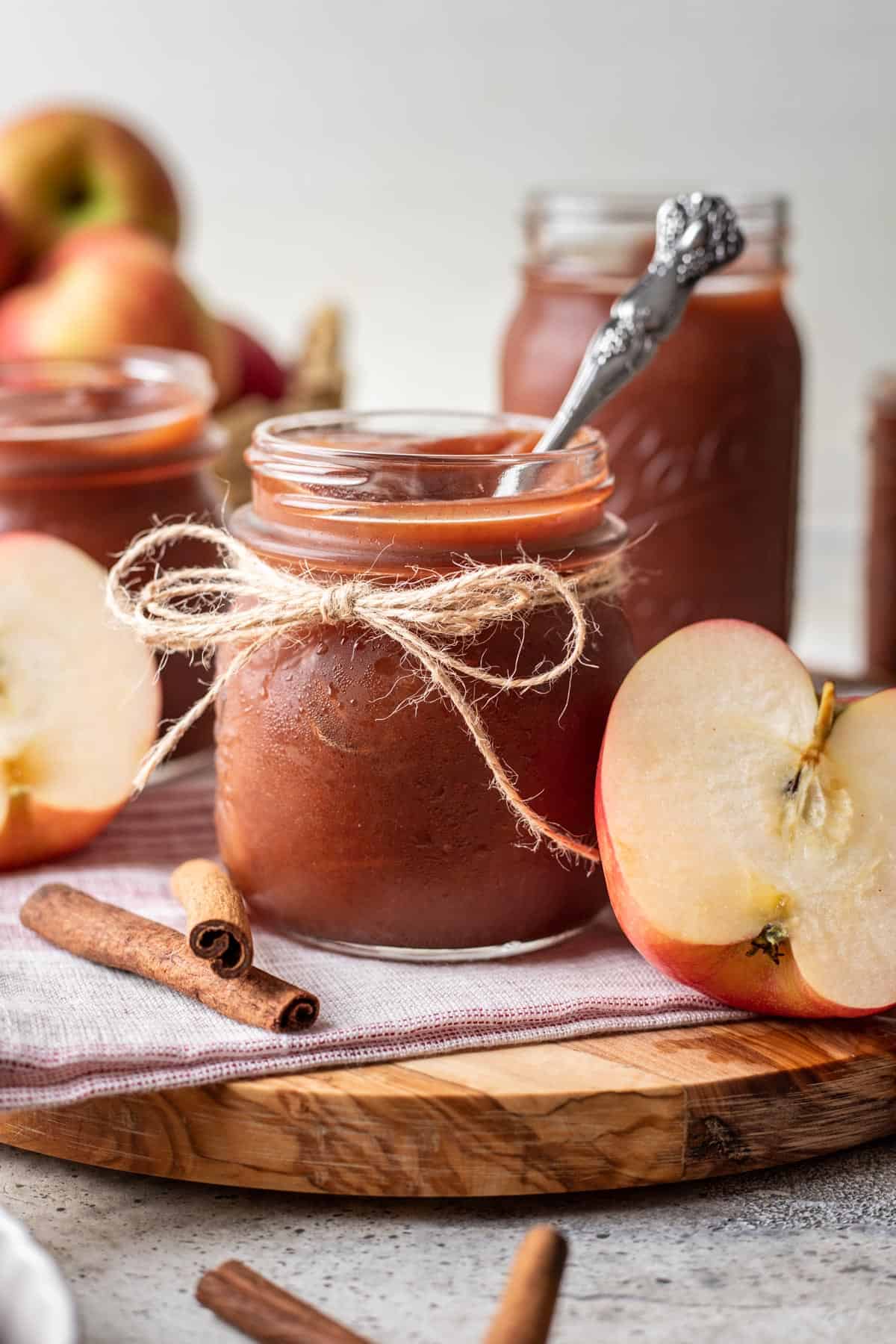 Instant pot apple butter in a jar with apples and cinnamon sticks around it.