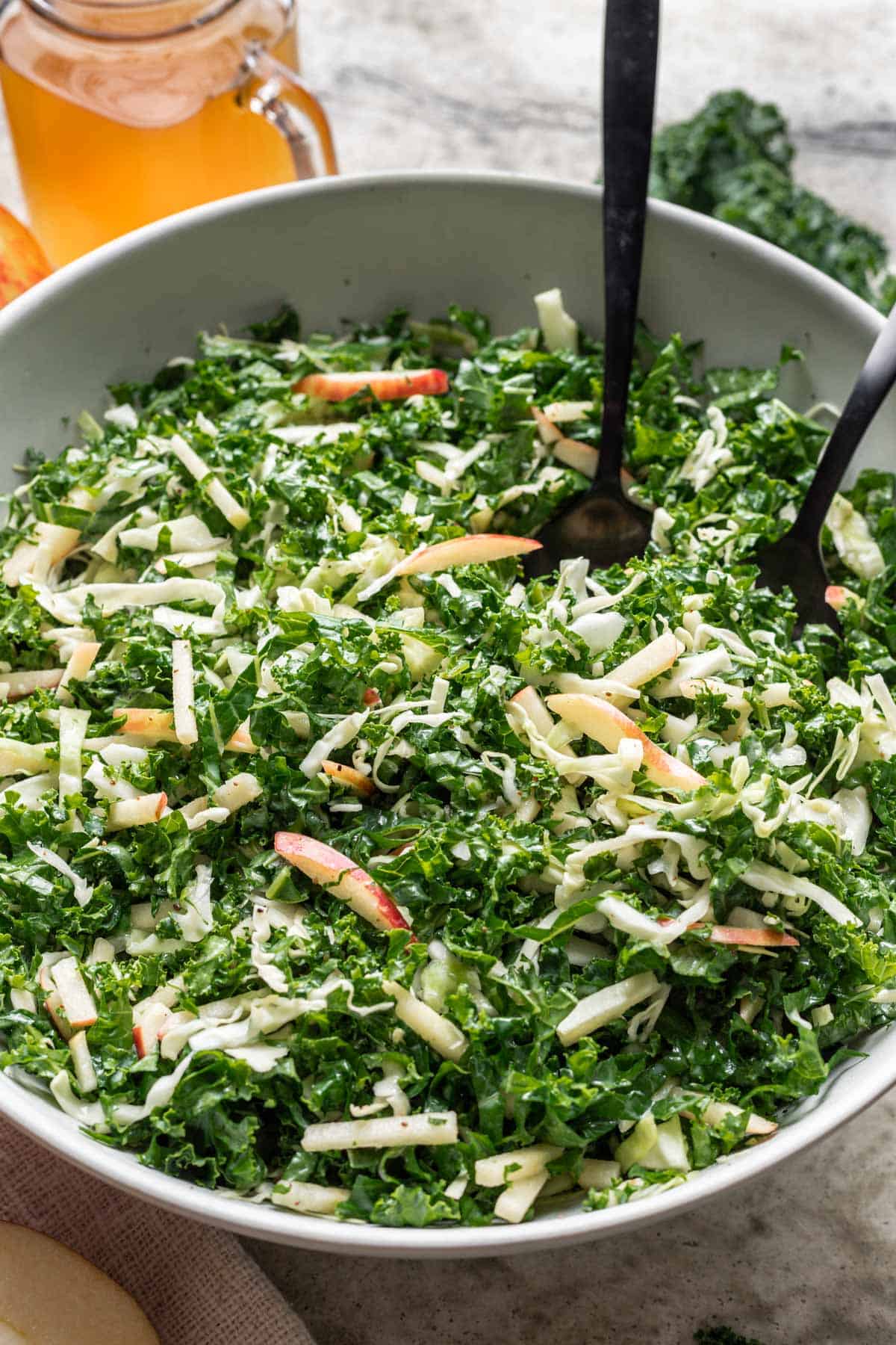 Kale apple slaw in a serving bowl with thinly sliced cabbage, apples, and green onions.