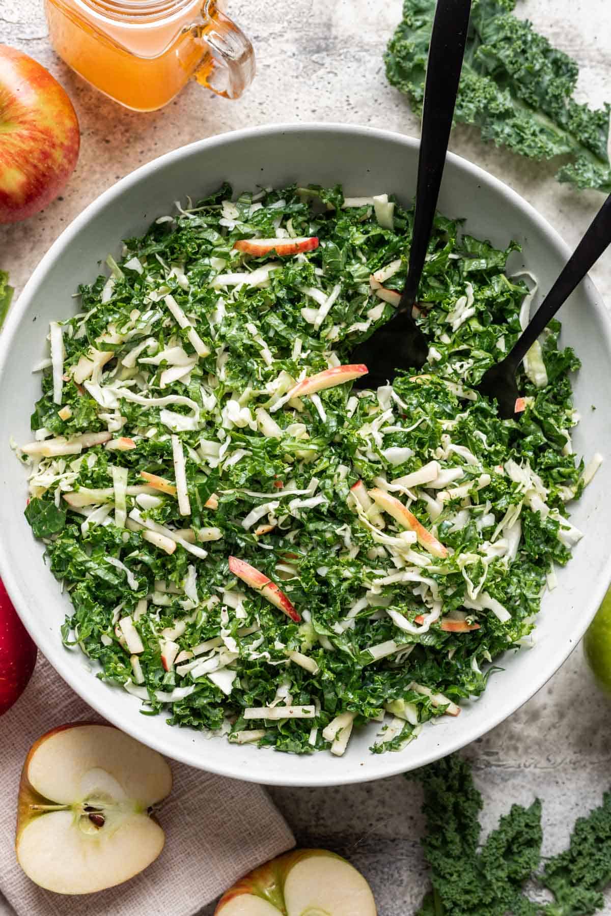 Kale apple slaw in a serving bowl with serving utensils.