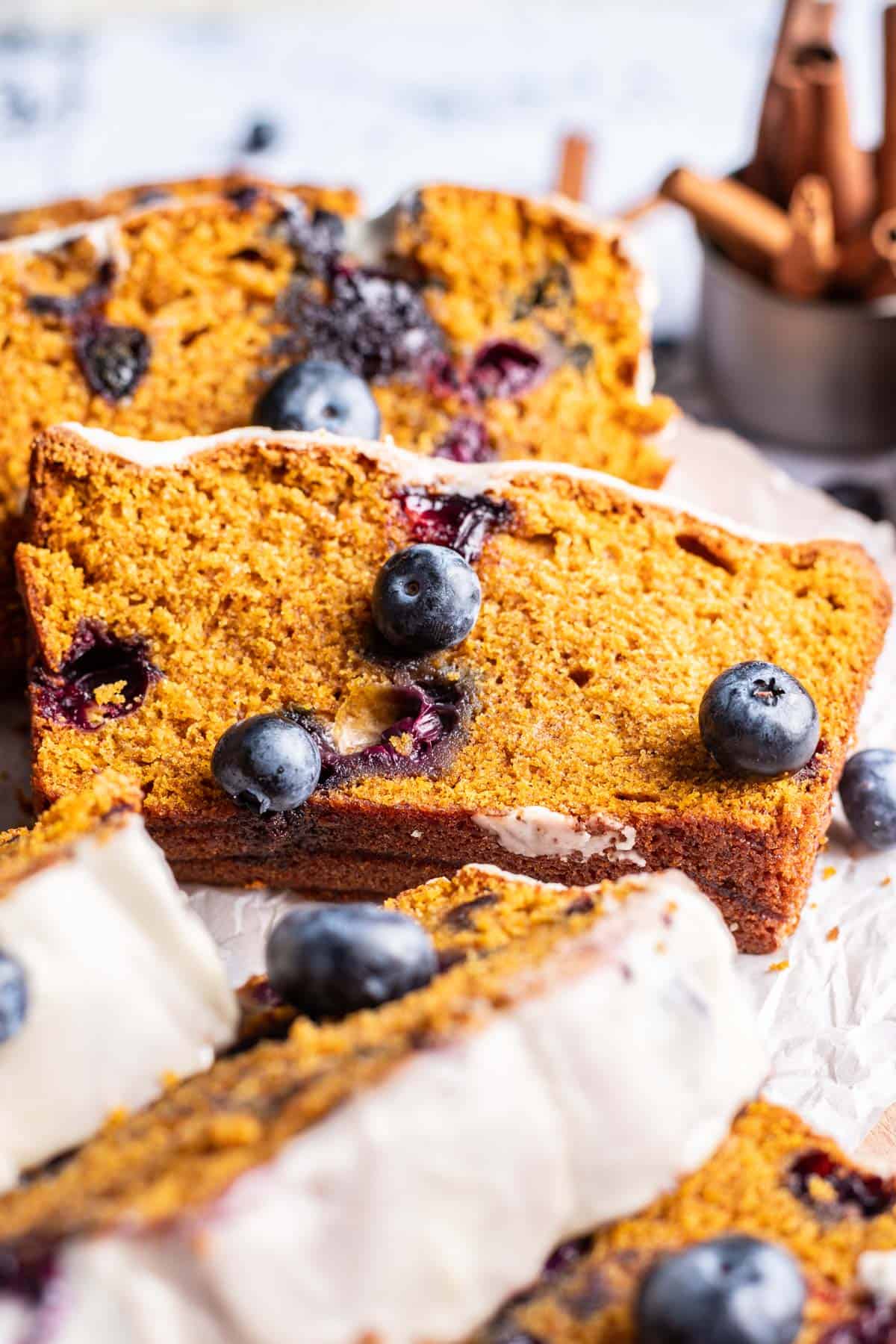 A slice of pumpkin blueberry bread on a serving tray with fresh blueberries.