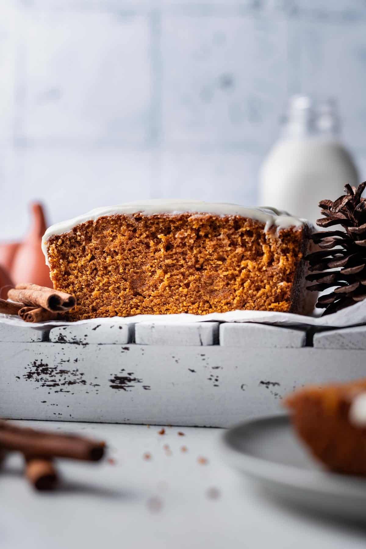 Loaf of pumpkin bread with cream cheese frosting on a white tray with cinnamon sticks and milk.