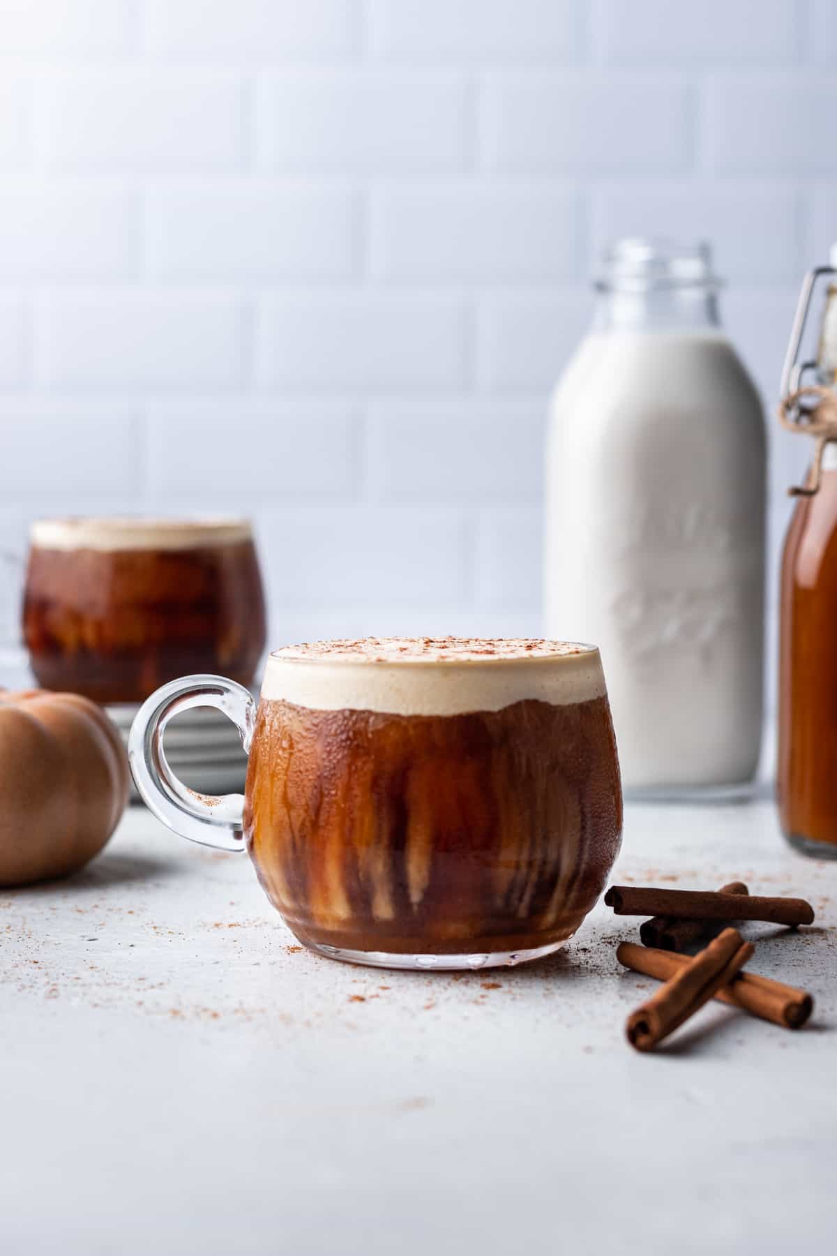 Pumpkin cream cold foam on a glass mug with a bottle of milk and simple syrup next to it.