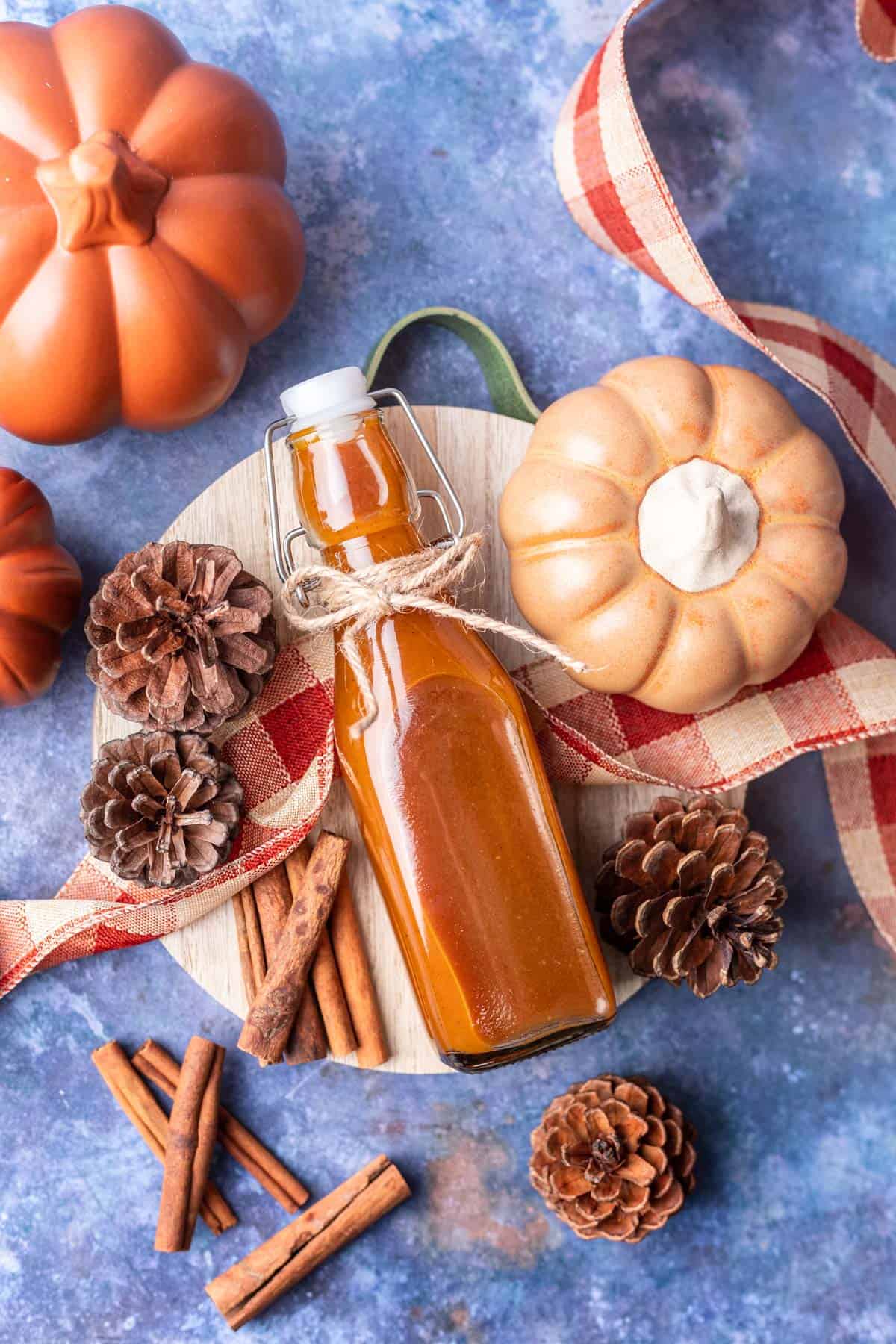 Pumpkin spice simple syrup in a bottle on a serving board with pinecones and pumpkins around it.