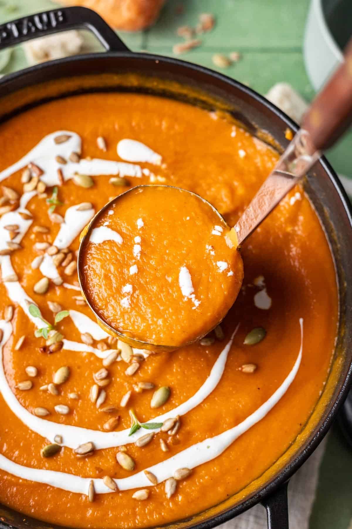 A ladle scooping out pumpkin, carrot, sweet potato soup to pour into a bowl.