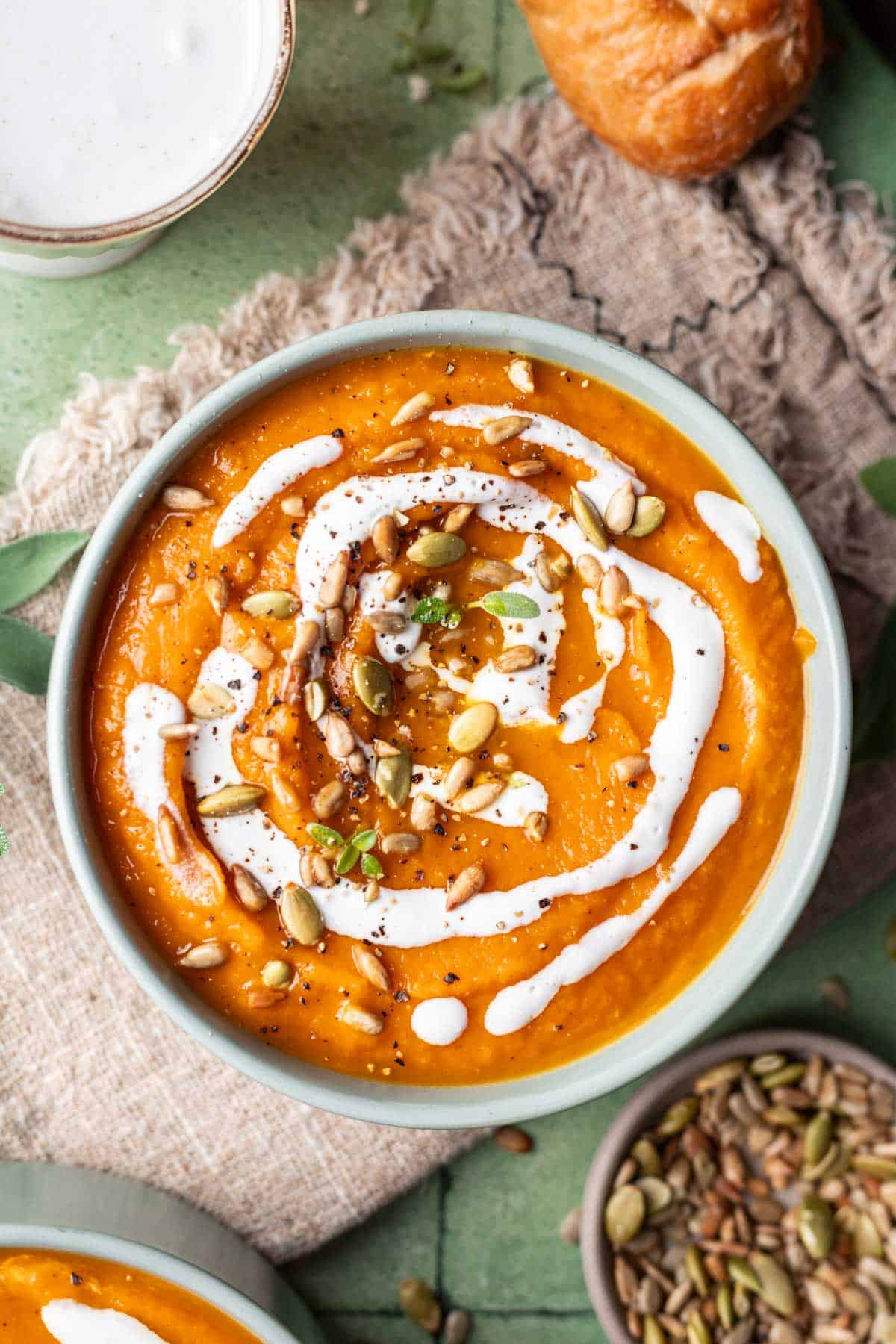 Pumpkin, carrot, and sweet potato soup in a green bowl drizzled with coconut cream on top.