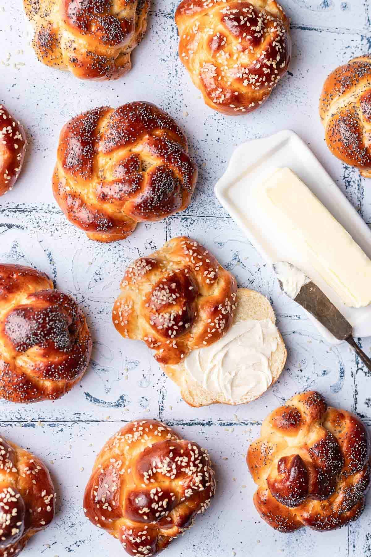 Challah buns topped with butter on a white tile backdrop.