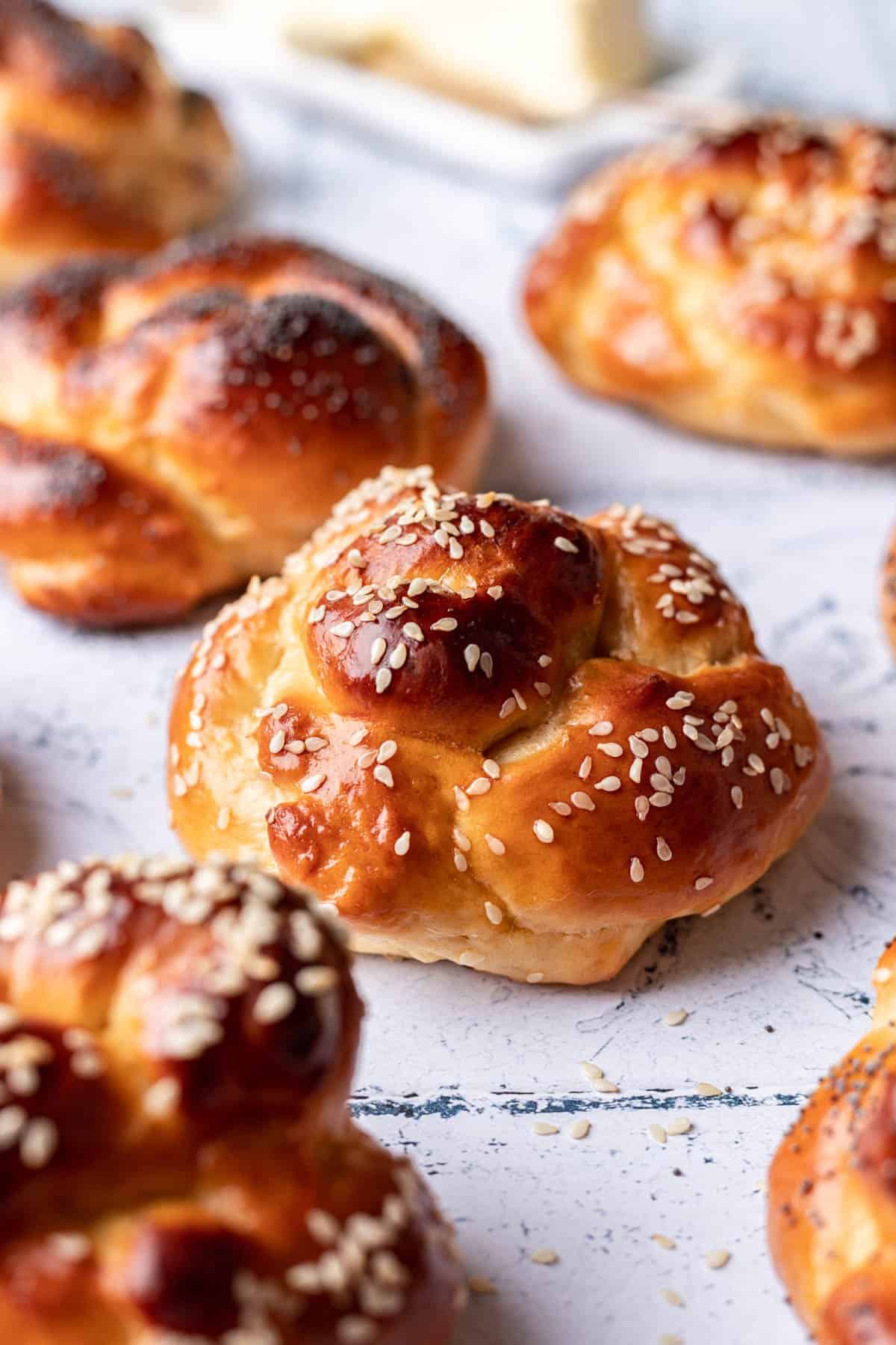 Challah rolls topped with sesame seeds on a tile backdrop.