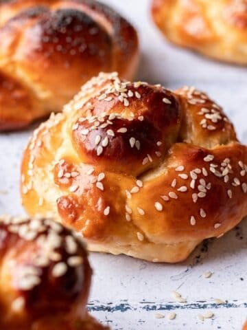 Challah rolls topped with sesame seeds on a tile backdrop.