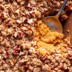 A serving spoon digging into sweet potato crunch casserole to show the creamy sweet potatoes and the crunchy topping.