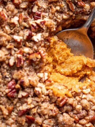 A serving spoon digging into sweet potato crunch casserole to show the creamy sweet potatoes and the crunchy topping.
