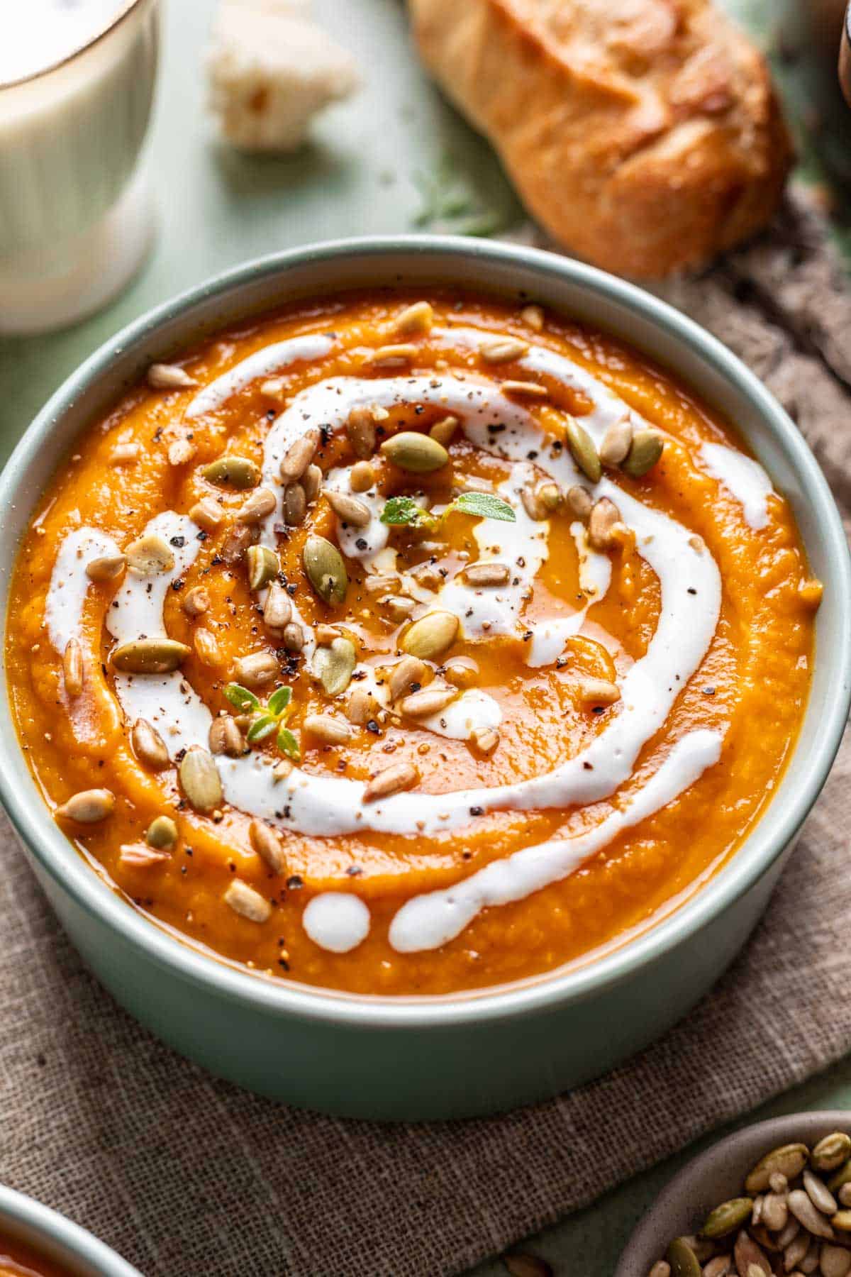 Pumpkin, carrot, and sweet potato soup in a bowl with coconut cream and pumpkin seeds on top.