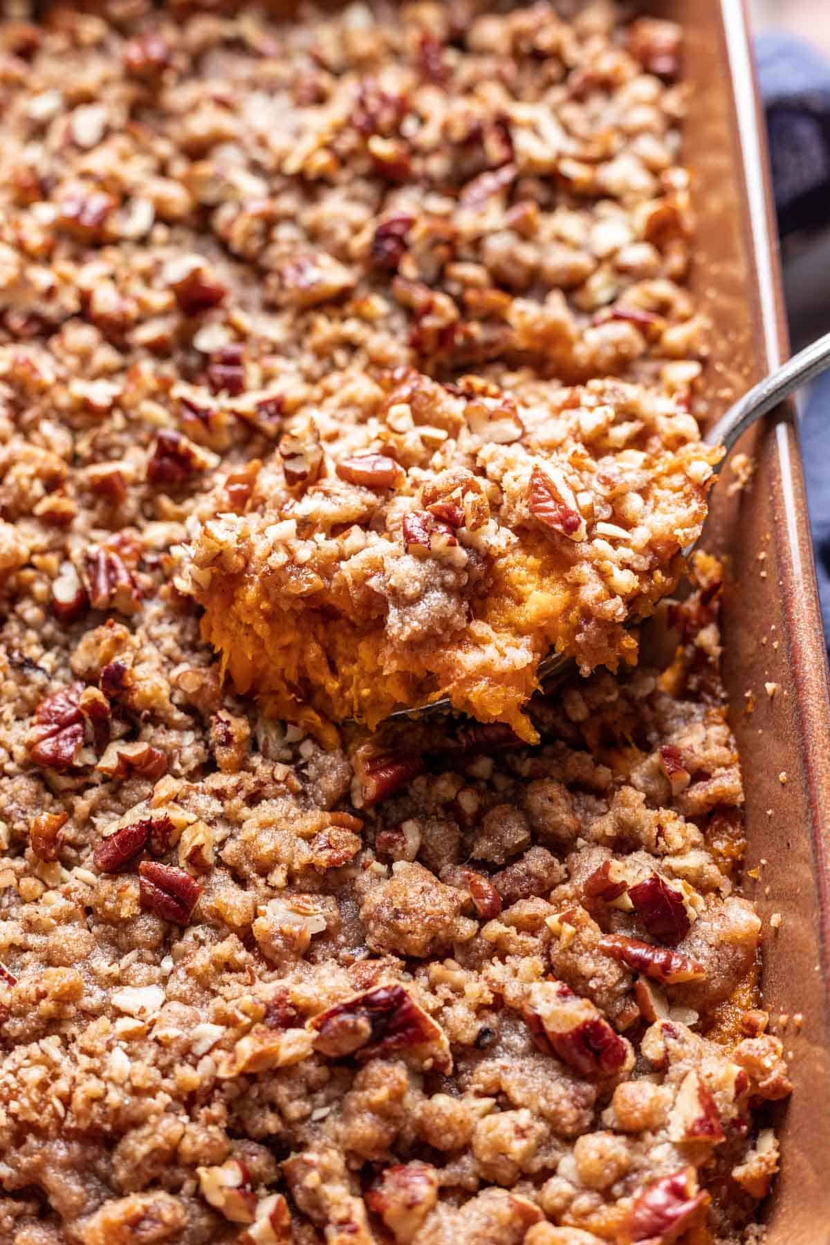 Sweet potato crunch casserole scooped out of the baking dish with a large spoon.