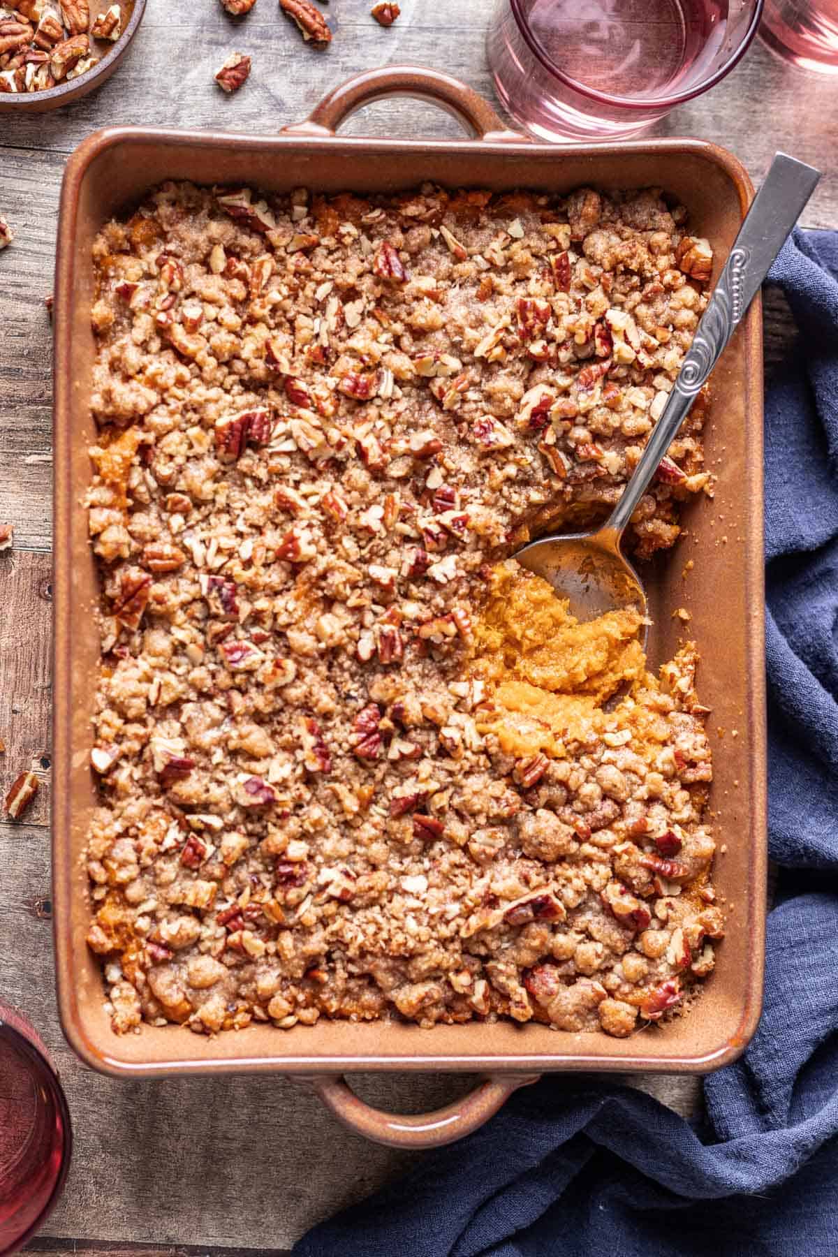 Sweet potato crunch casserole in a brown baking dish with a spoon scooping some out.