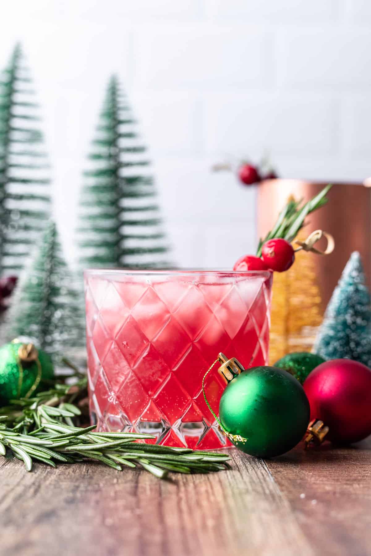 Christmas moscow mule in a glass cup with mini ornaments and pine trees around it.