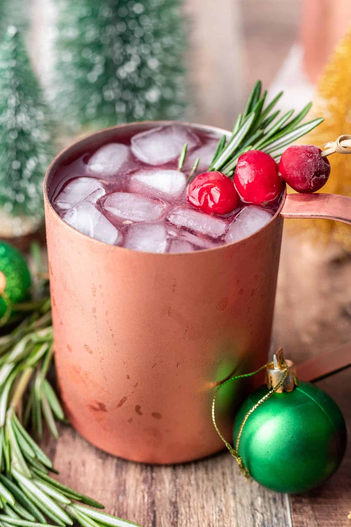 Christmas moscow mule in a copper mug with lots of ice, fresh cranberries, and rosemary.