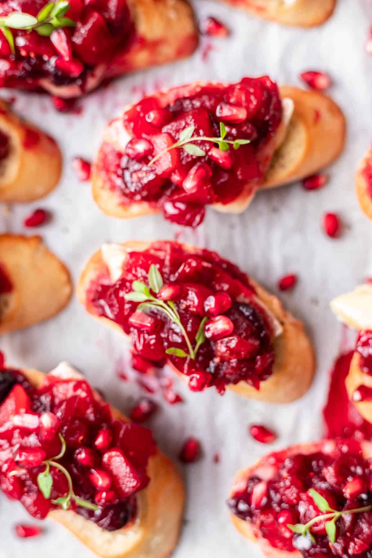 Cranberry brie crostini on a platter with pomegranate seeds, cranberry compote, and fresh thyme.