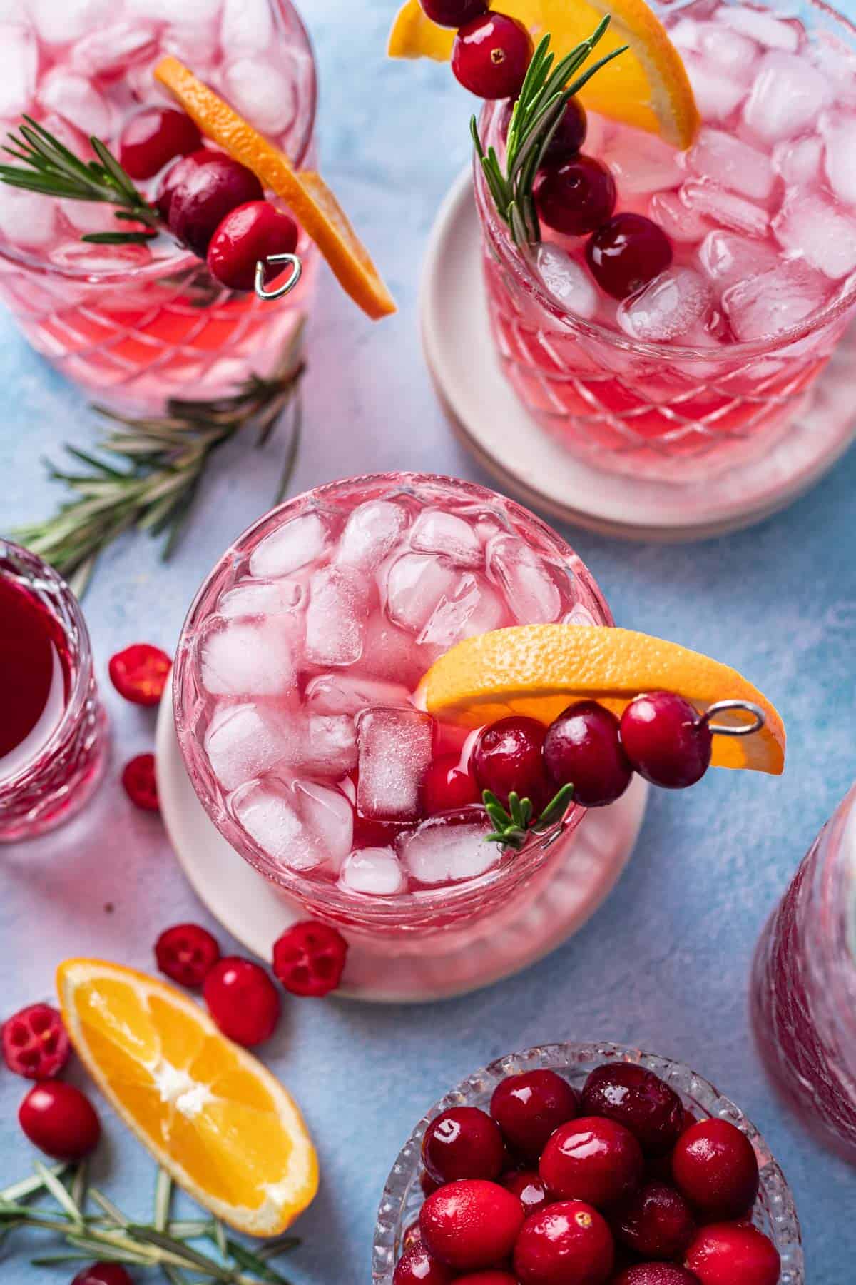 Cranberry gin and tonic garnished with an orange wedge, fresh cranberries, and rosemary.