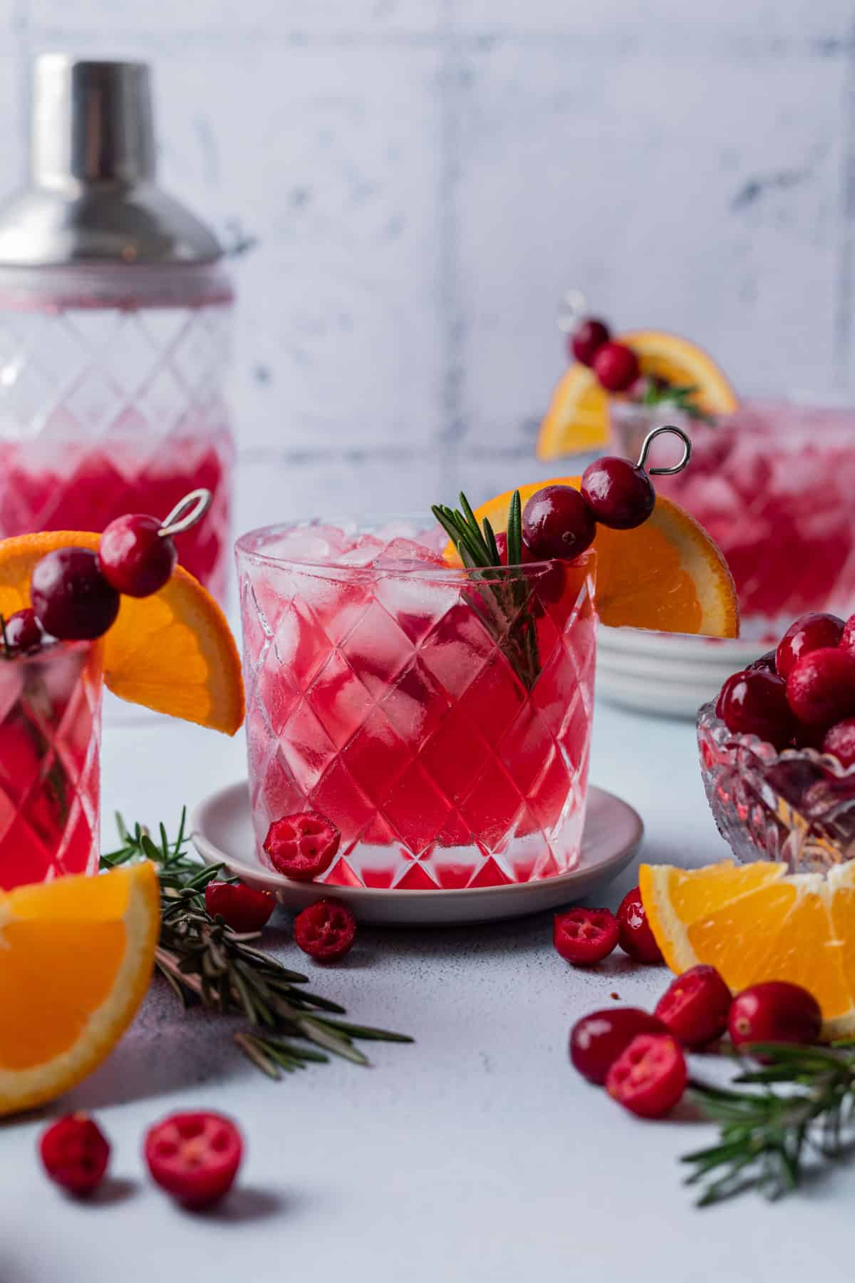 Cranberry gin cocktail in a glass with fresh cranberries, rosemary, and an orange slice.