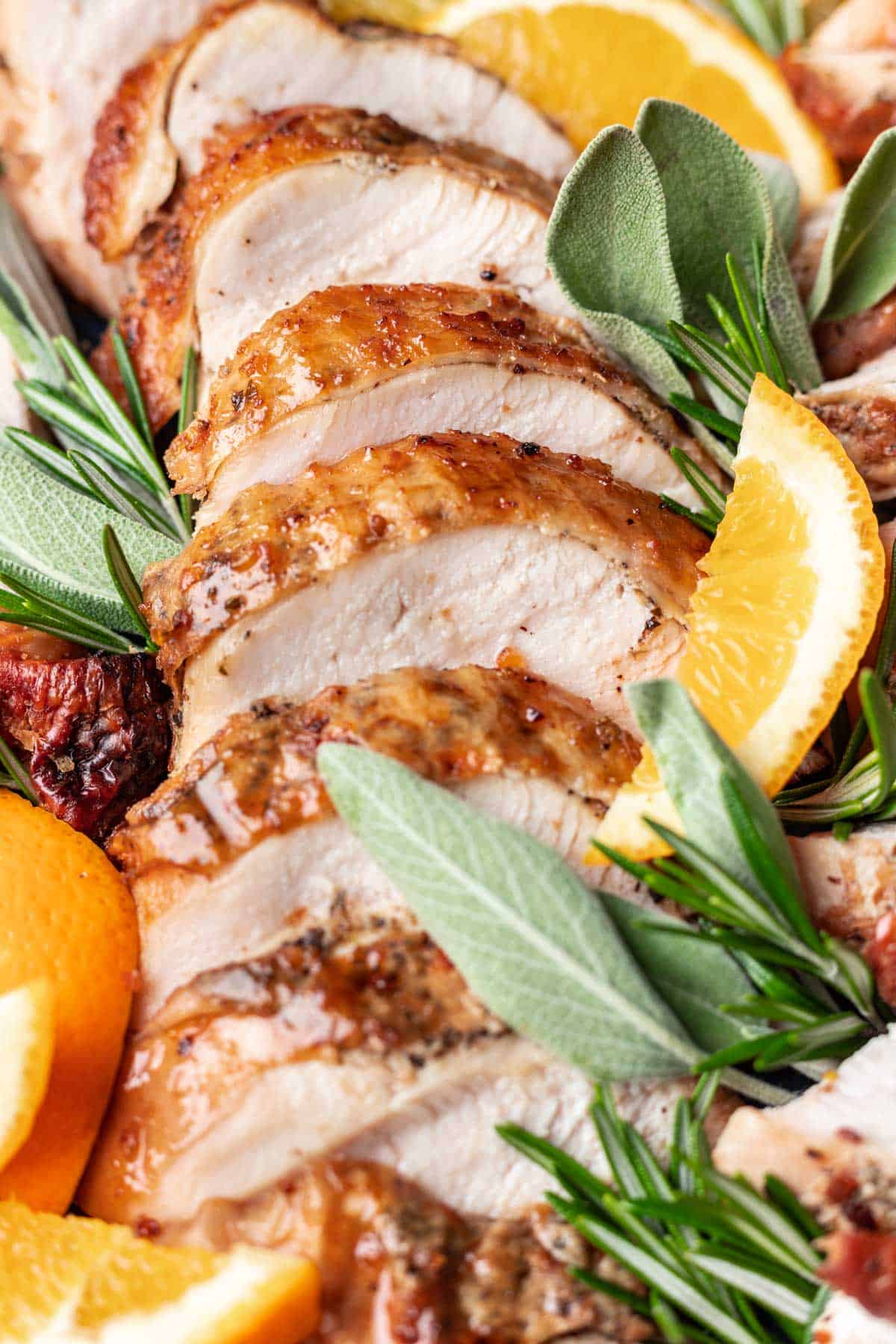 Sliced dutch oven turkey breast with golden brown skin on a platter with oranges, sage, and rosemary.