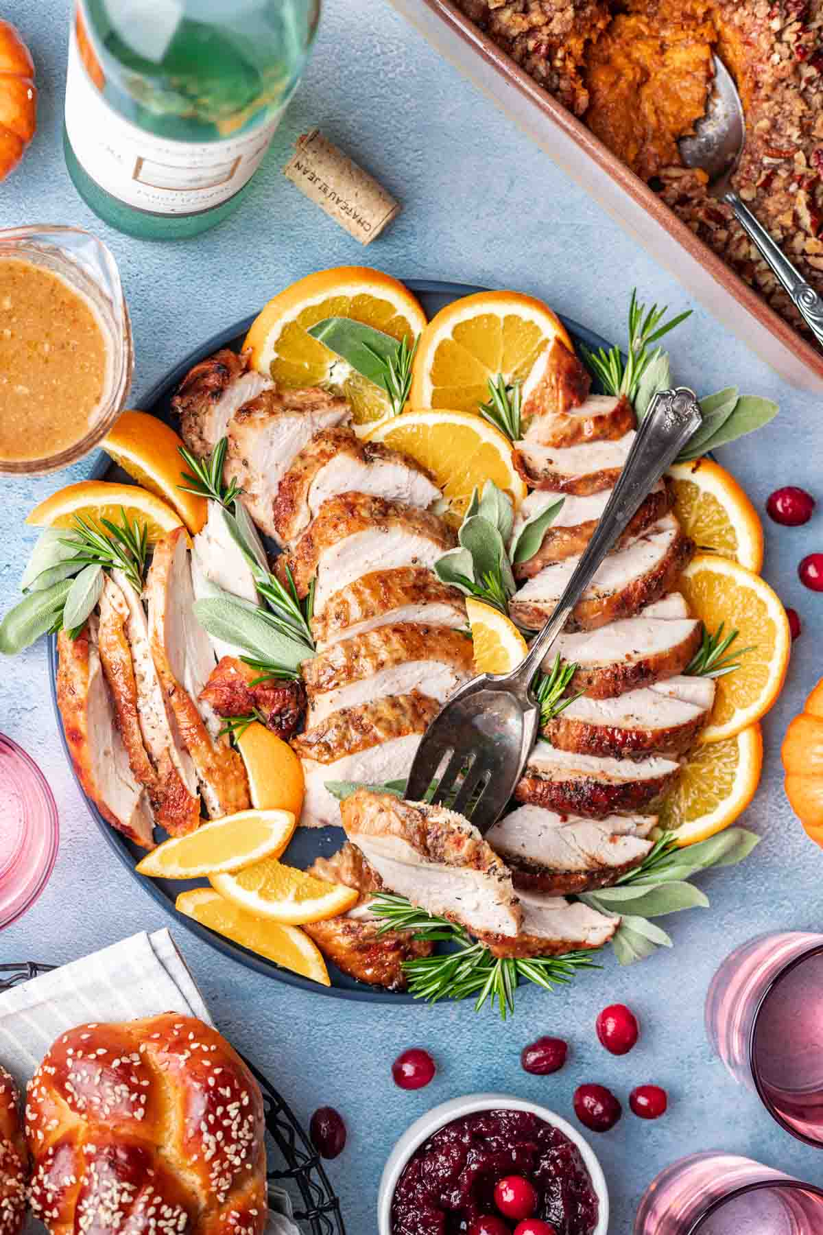 Sliced dutch oven turkey breast on a serving platter with sliced oranges, fresh herbs, and a serving fork.