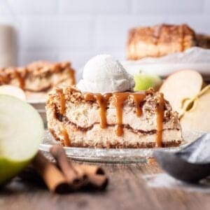 A slice of apple crumble cheesecake on a glass plate, topped with vanilla ice cream.