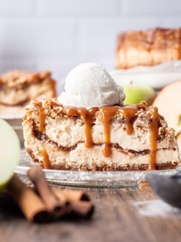 A slice of apple crumble cheesecake on a glass plate, topped with vanilla ice cream.