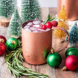 Christmas moscow mule in a copper mug garnished with fresh rosemary and cranberries.