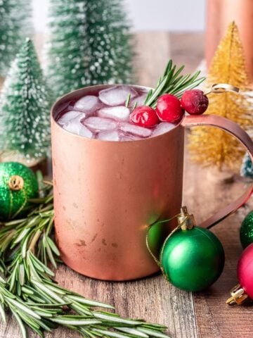 Christmas moscow mule in a copper mug garnished with fresh rosemary and cranberries.