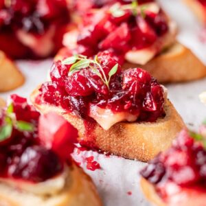 Cranberry brie crostini on a piece of parchment paper garnished with thyme.