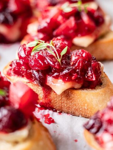 Cranberry brie crostini on a piece of parchment paper garnished with thyme.