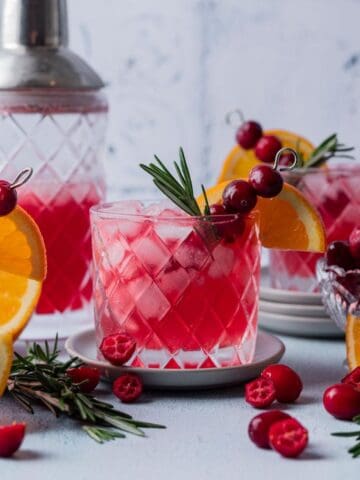 Cranberry gin cocktail in a glass garnished with fresh cranberries, an orange slice, and fresh rosemary.