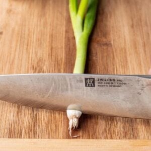 A scallion being sliced on a cutting board.