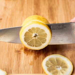 A sharp knife cutting lemon slices on a cutting board.