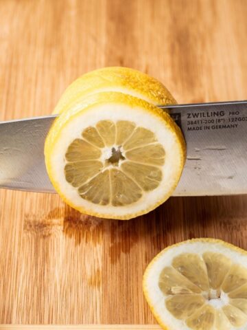 A sharp knife cutting lemon slices on a cutting board.